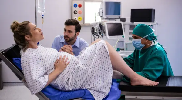 Kobieta w ciąży na fotelu porodowym, wspierana przez partnera i lekarza.