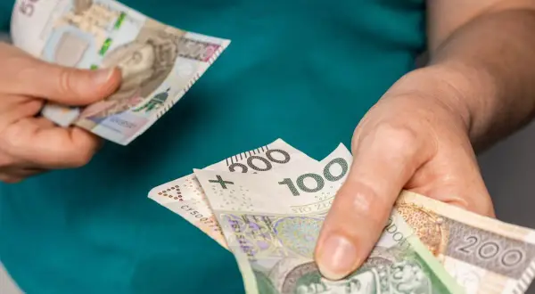 Dłonie trzymają polskie banknoty o nominałach 100, 200 i 500 zł.